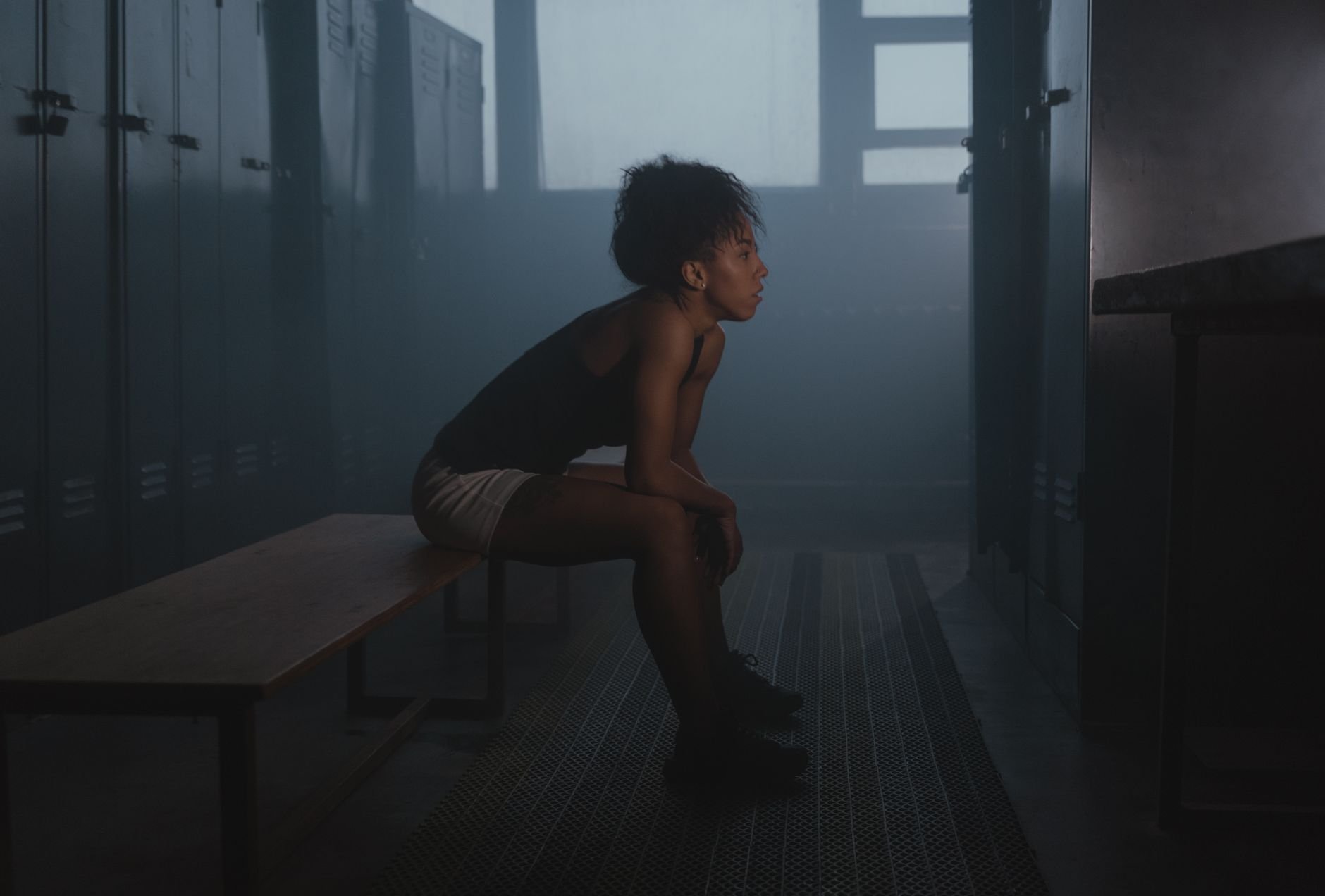 Woman sitting on a bench in a dimly lit locker room, in a quiet, reflective moment
